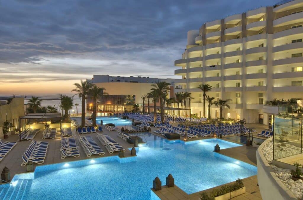 Piscina do db San Antonio Hotel + Spa All Inclusive cercado por espreguiçadeiras e coqueiros, para representar hotéis em Malta