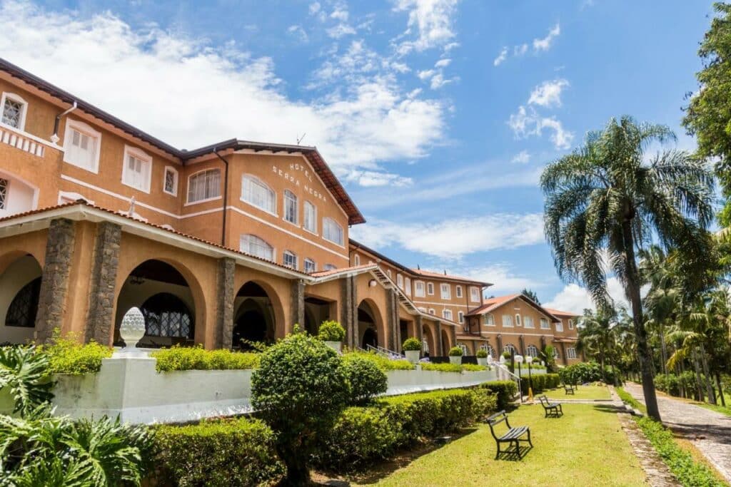Ampla propriedade do Grand Resort Serra Negra com uma construção em estilo colonial antigo e com um jardim na frente com arbustos e plameiras