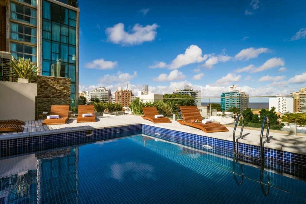 Piscina no Own Montevideo com um deck dando vista para os prédios com algumas espreguiçadeiras, para representar os hotéis em Montevidéu