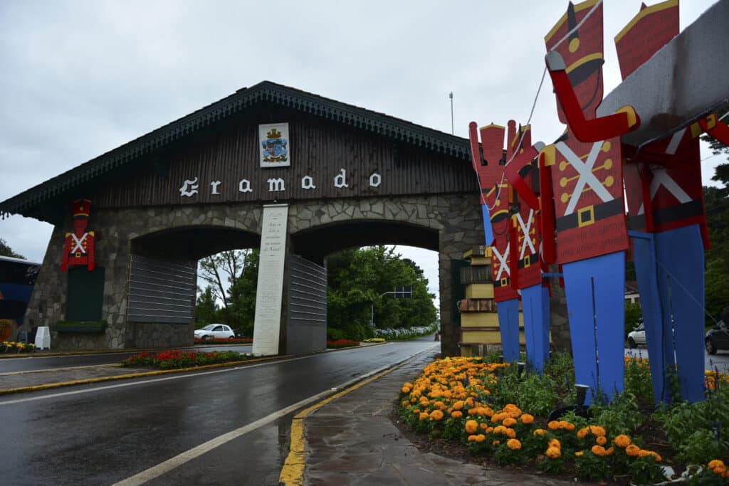 Portal de Gramado, com soldados de madeira do lado e flores amarelas e vermelhas nos canteiros