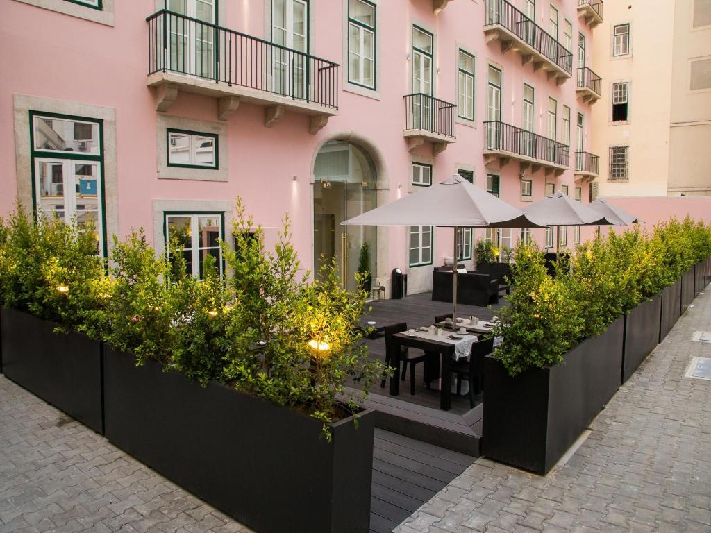 Parte da fachada do Portugal Boutique Hotel, com paredes rosa claro, sacadas de ferro e janelas amplas, além de mesas com guarda-sóis numa área na frente da entrada