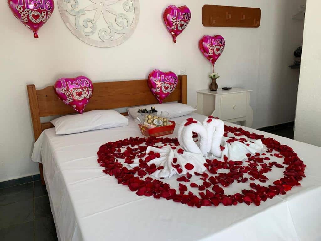 Quarto da Pousada Cachoeira inteiro decorado para um casal com bexigas em formato de coração, pétalas de rosa sob a cama de casal e uma cesta com bombons