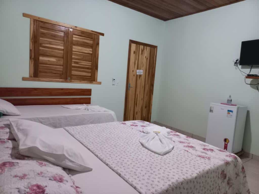 Quarto da Pousada do Nondas, com uma cama de casal, uma cama de solteiro, um frigobar, TV na parede, e janela e porta de madeira