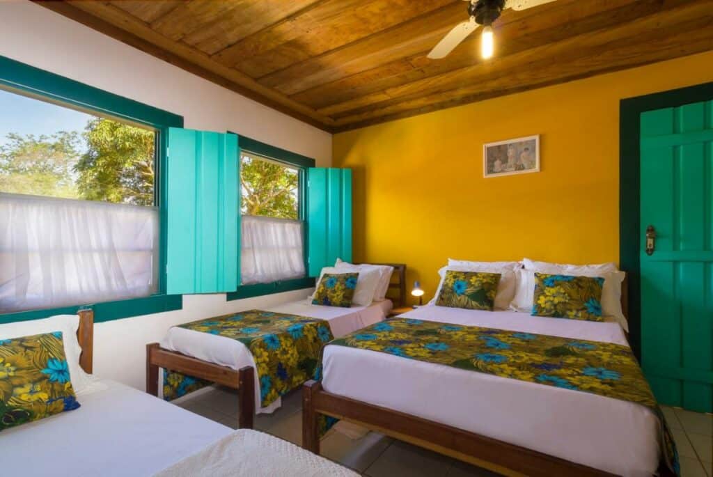Quarto da Pousada Vila do Porto com uma cama de casal, uma de solteiro, tudo decorado em tons de verde e amarelo, a roupa de cama é florida