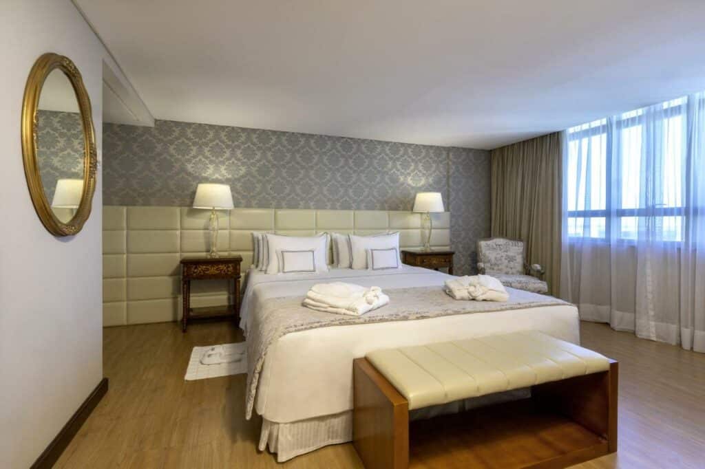 Quarto do Meliá Brasil 21 com uma cama de casal, chão de madeira, decoração de época, tudo em tons de bege, branco e cinza