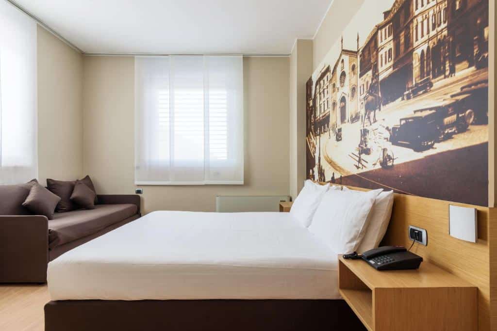quarto com cama de casal, sofá, janela e papel de parede, móveis de madeira no B&B Hotel Milano La Spezia