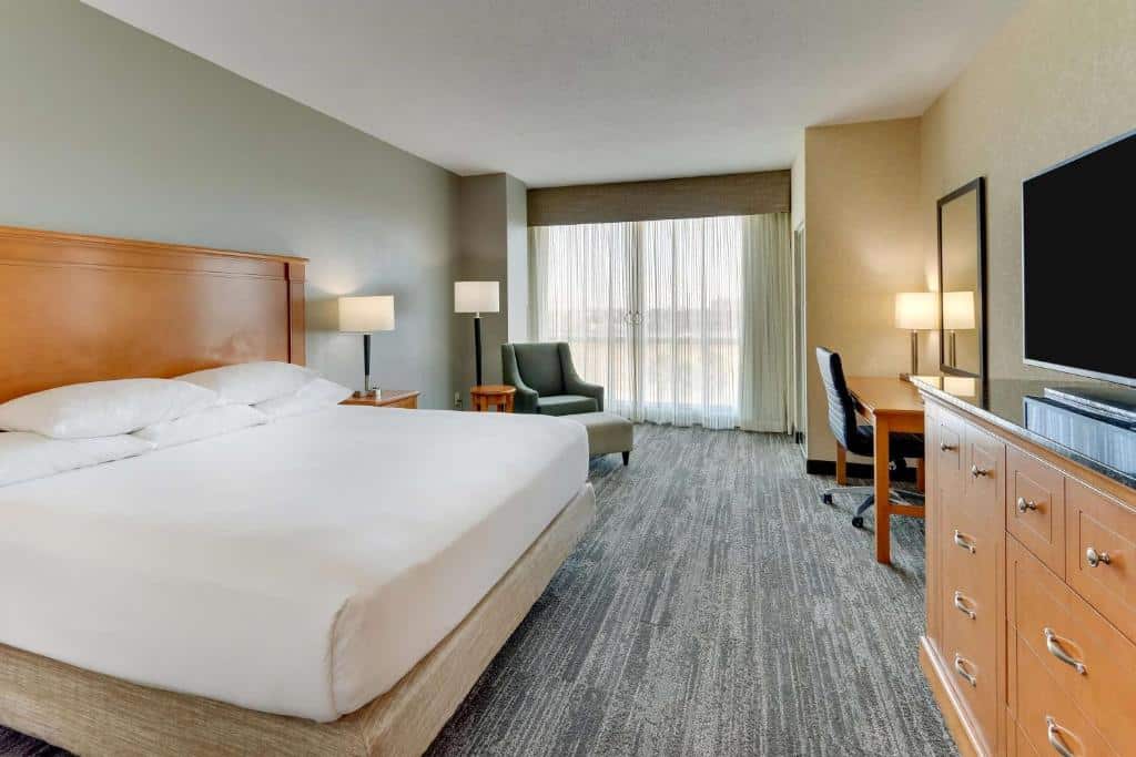 quarto com cama de casal, janela grande, balcão, tv e poltrona no Drury Inn & Suites Orlando near Universal Orlando Resort