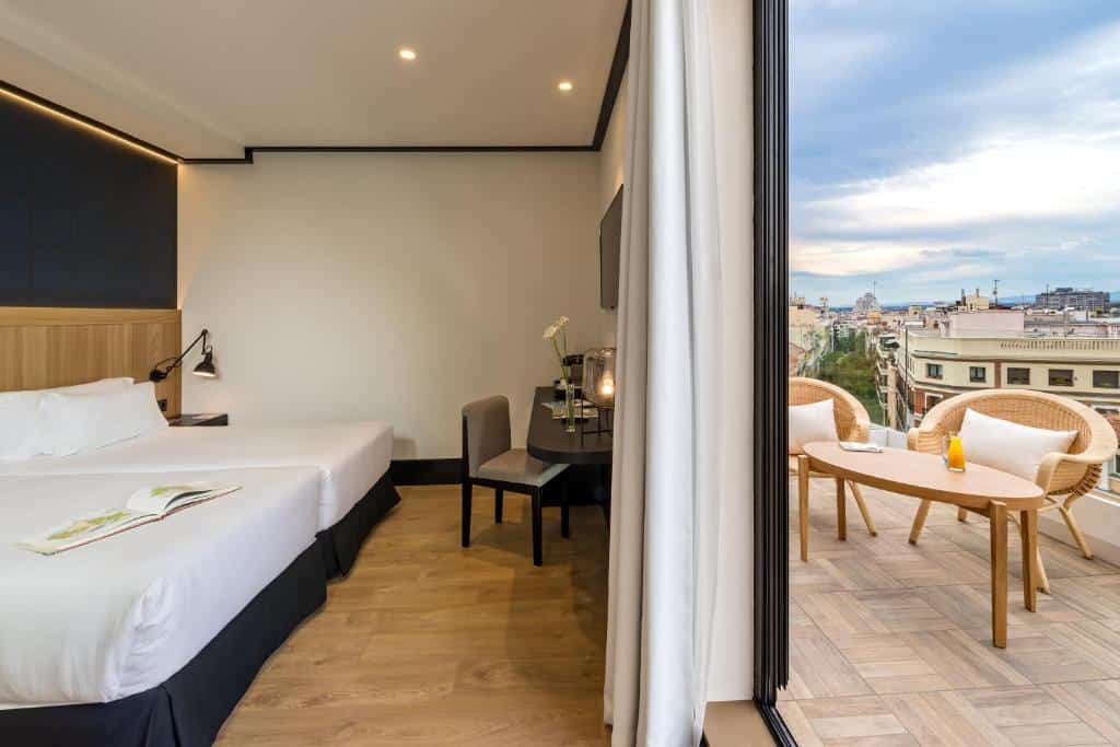 vista dividida do quarto com duas camas e tv e do outro lado a varanda com mesa e cadeiras e vista no H10 Puerta de Alcalá