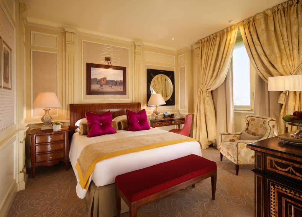 quarto requintado com decoração em tons de dourado e vermelho, com cortina, cama grande, janela e móveis de madeira no Hotel Principe Di Savoia - Dorchester Collection