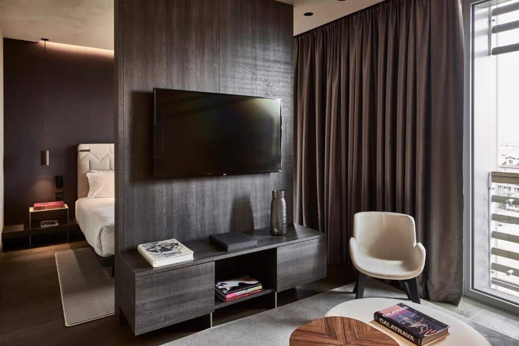 quarto dividido entre a cama e um painel com tv e, do outro lado, mesa e cadeiras no Hotel VIU Milan um dos hotéis em Milão