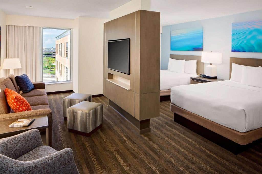 quarto grande separado pela tv, com duas camas de um lado e do outro sofás com janela do Hyatt House across from Universal Orlando Resort um dos hotéis em Orlando