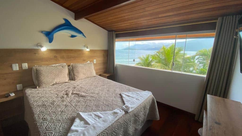quarto com cama de casal e vista de uma janela triangular da praia na Kaliman Pousada