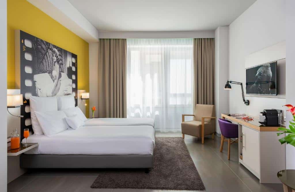 quarto com cama e janela grandes, tv e parede e poltrona amarelas no NYX Hotel Milan by Leonardo Hotels
