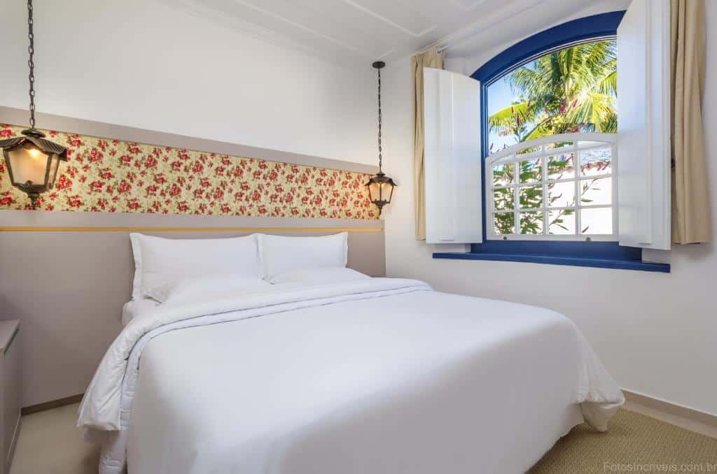 quarto com cama de casal e janelinha com borda azul e detalhes vermelhos na parede na Pousada Aconchego