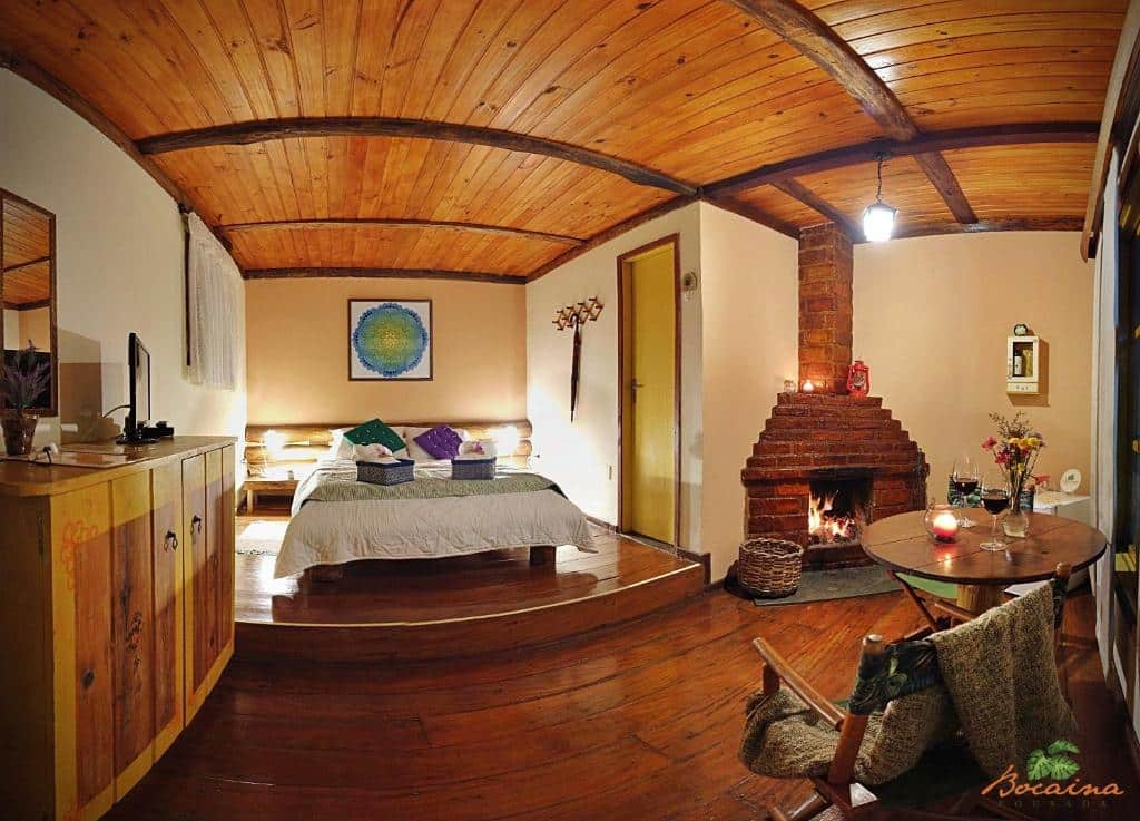 quarto amplo com cama de casal, lareira e móveis de madeira na Pousada Bocaina