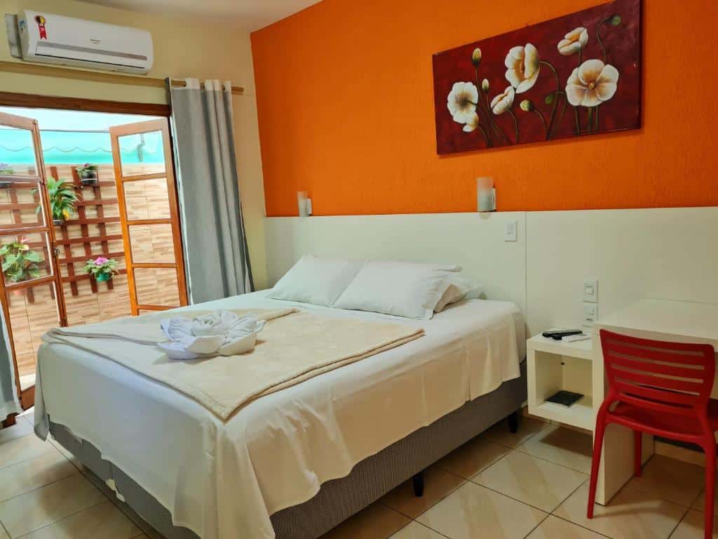 quarto com cama de casal, parede laranja por porta grande de madeira com umas plantinhas na Pousada Recanto