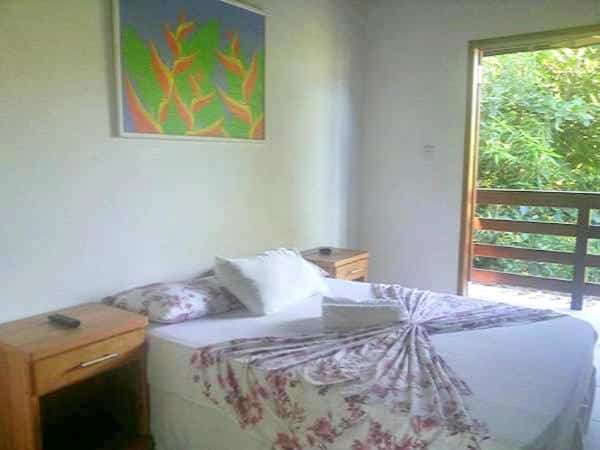 quarto com cama de casal e vista da sacada para natureza na Pousada Sol da Trindade com tela na parede e móveis de madeira
