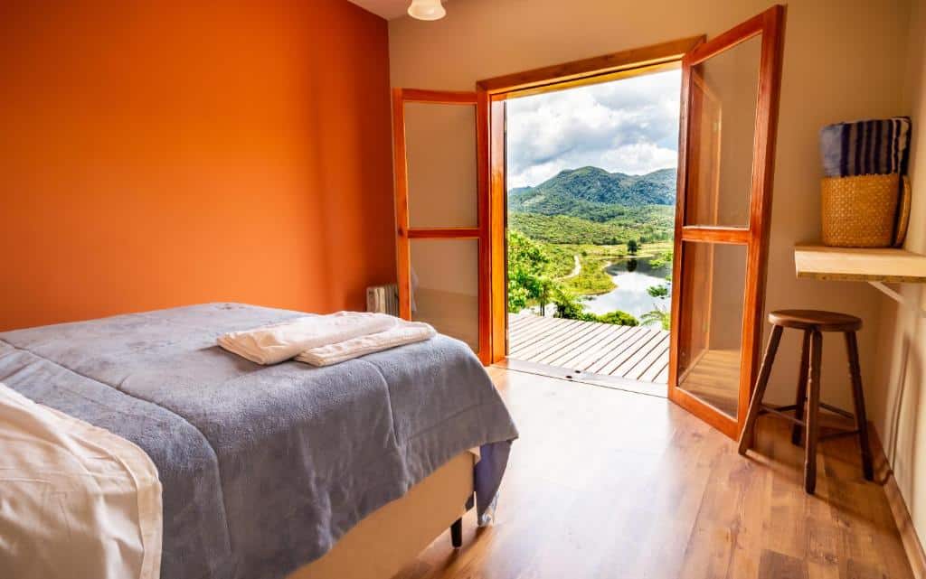quarto com cama e porta grande de madeira com vista para a serra verde com montanhas de fundo na Villas da Bocaina
