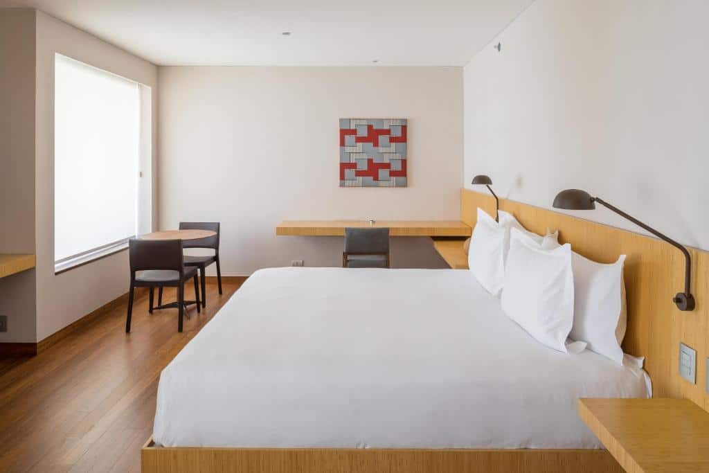 Quarto no B Hotel Brasilia com decoração bem clean, chão de madeira, cama de casal, uma mesa de escritório com uma cadeira, uma mesinha com duas cadeiras, para representar hotéis em Brasília