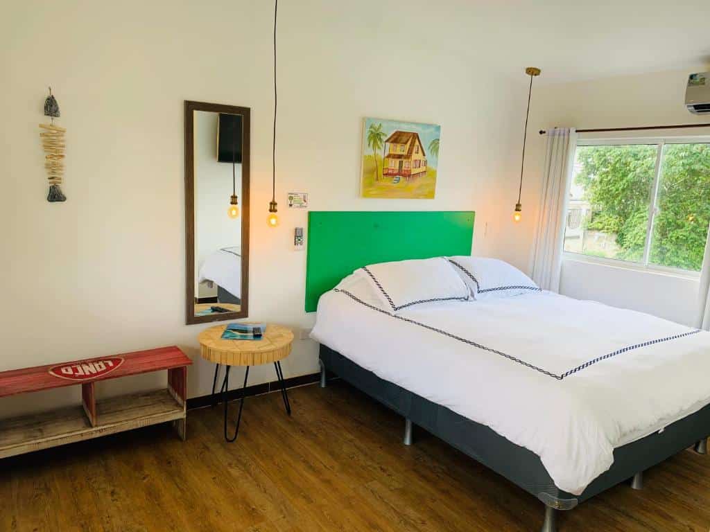 Quarto no Be Happy Hotel com uma cama de casal, uma janela com cortinas, um espelho, uma mesinha de madeira e lâmpadas em estilo luminária penduradas no teto