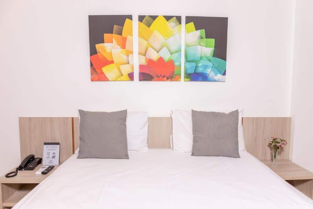 Quarto no Cancún Hotel by H Hotéis - Airport com uma cama de casal com almofadas e travesseiros brancos e cinzas, uma mesa de cabeceira, e um quadro colorido sob a cama