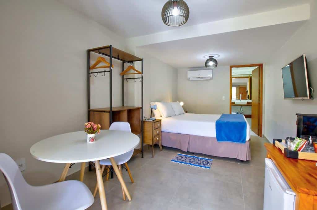 Quarto amplo no Filimahalo Hotel com uma cama de casal, um ar-condicionado, banheiro, televisão, frigobar, armário de conceito aberto, uma pequena mesa com duas cadeiras, e duas pequenas cômodas com luminárias nas laterais da cama