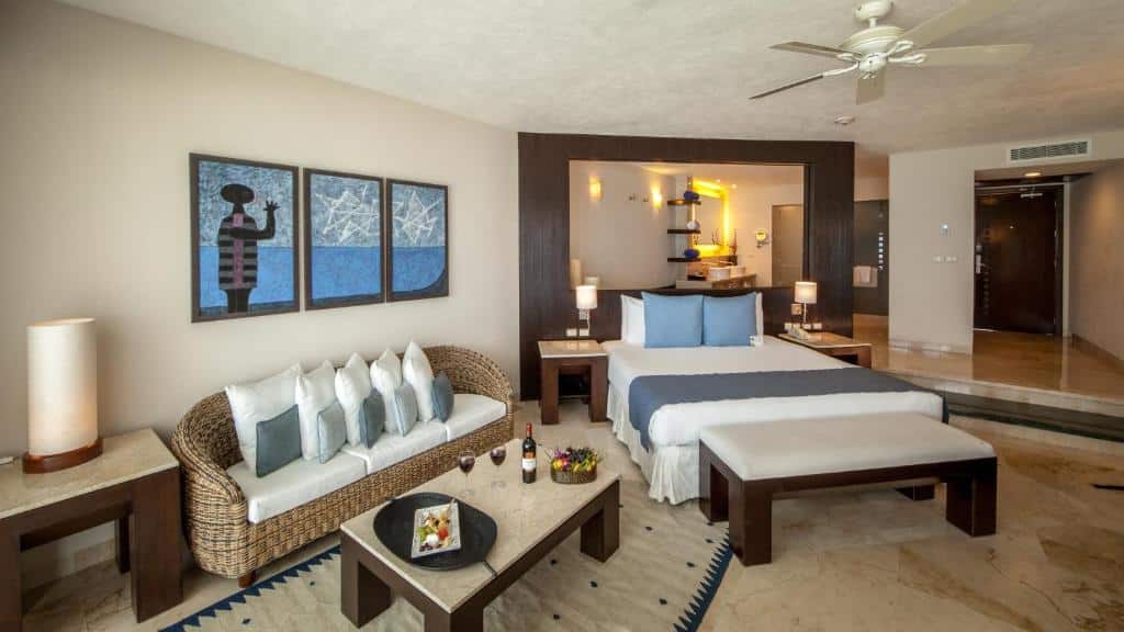 quarto do Grand Park Royal Cancún com uma cama de casal, um amplo espelho na cabeceira, uma área de estar e um ventilador de teto