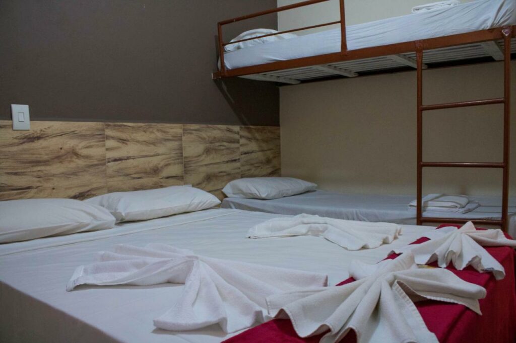 Quarto do Hotel Fazenda Estância São Domingos com uma cama de casal e uma beliche, as roupas de cama são vermelhas e brancas