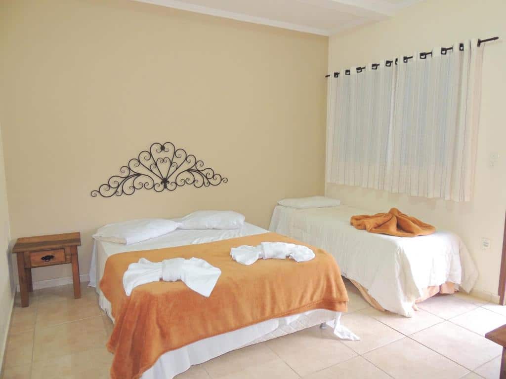 Quarto do Hotel Fazenda Villa Verona com uma cama de casal, uma cama de solteiro, uma janela com cortinas, para representar hotéis em Serra Negra