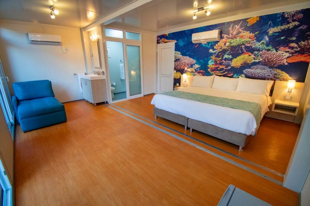 Quarto muito amplo no Hotel Reina del Mar By Dorado com uma cama de casal, um ar-condicionado, uma poltrona, chão de madeira, um frigobar, um banheiro privativo e uma sacada ampla, para representar onde ficar em San Andres
