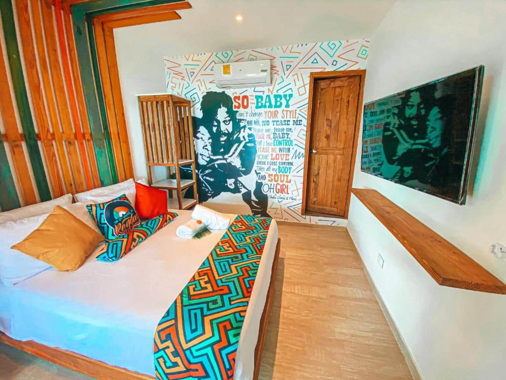 Quarto no In Di House of Reggae Boutique com uma decoração fazendo referência ao reggae, uma cama de casal, um ar-condicionado, uma televisão e um armário de conceito aberto, tudo em tons de madeira, azul, amarelo, verde e vermelho