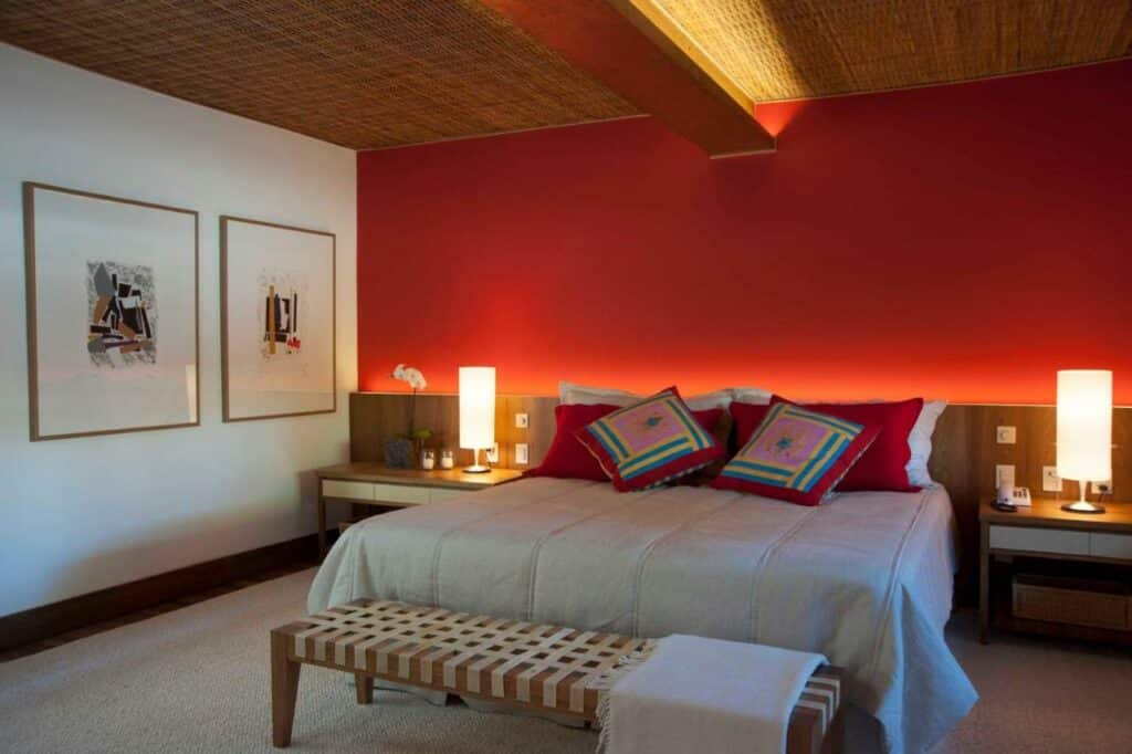 Quarto amplo na Pousada Literária de Paraty com uma parede vermelha, com uma cama de casal, uma cabeceira de madeira com dois abajures