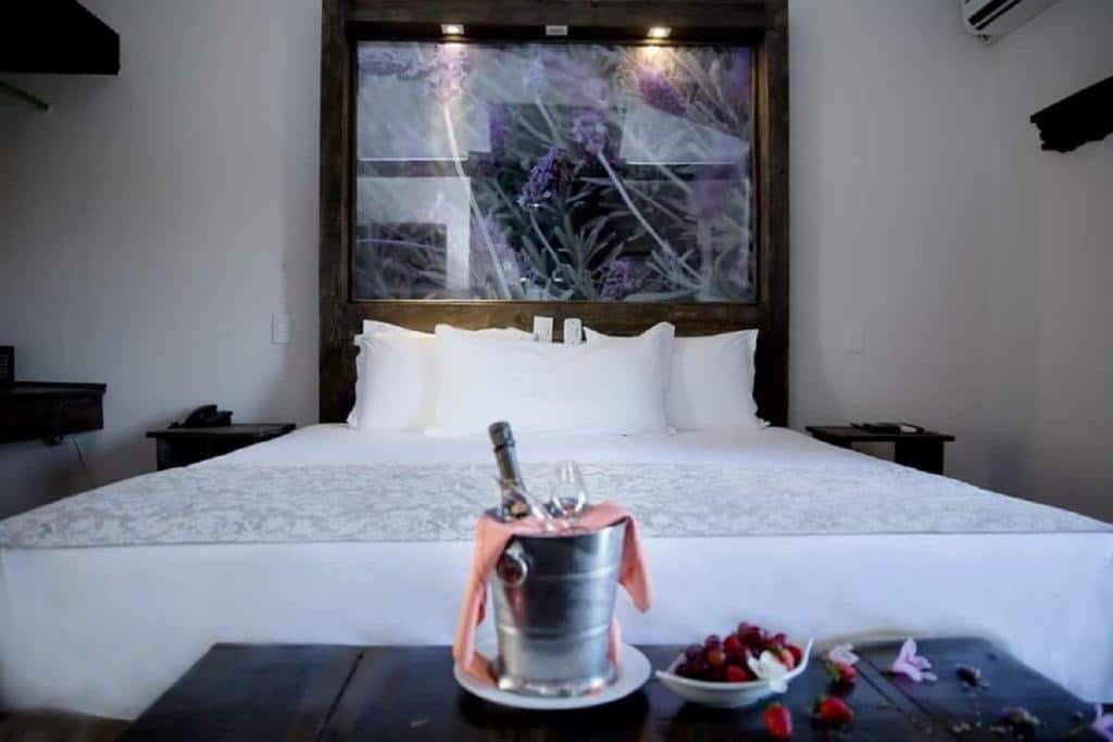 Quarto do Hotel Pousada Shangri-la com uma cama de casal, um quadro atrás da cabeceira e uma pequena mesa com vinho e taças