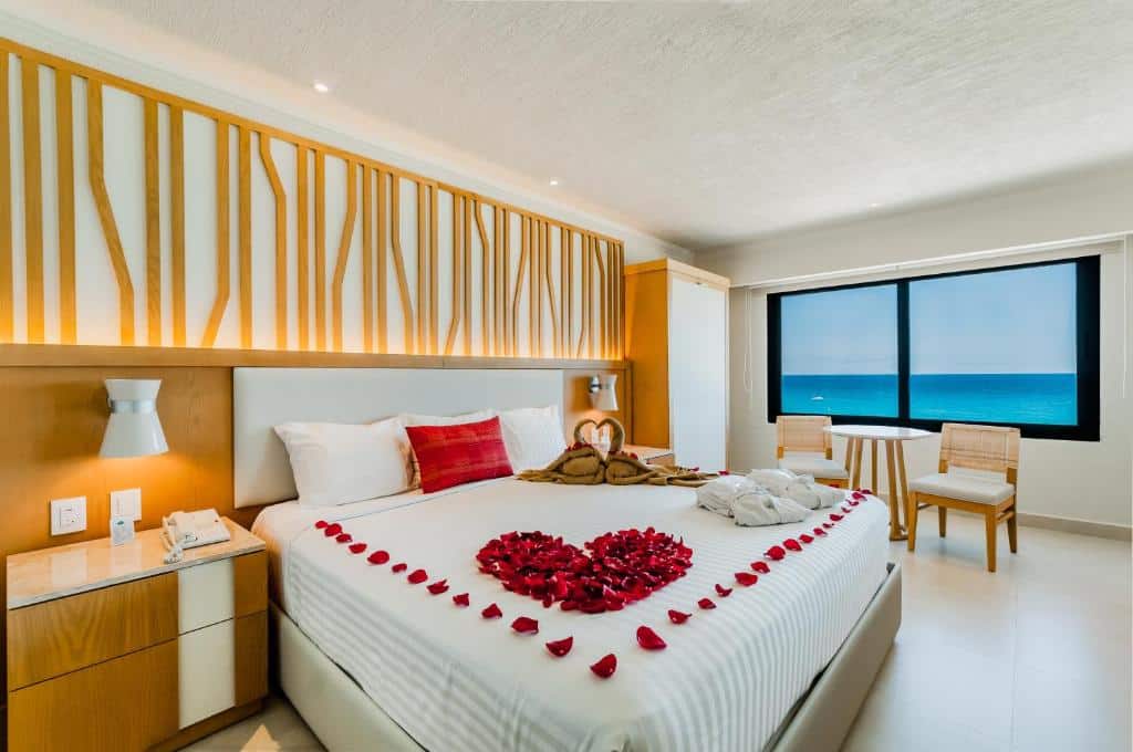 suíte do Royal Solaris Cancun com uma cama de casal enfeitada com pétalas de rola e uma janela com vista para o mar ao fundo