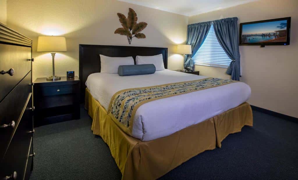 Quarto do Sailport Waterfront Suites com uma cama de casal, uma cômoda, duas mesinhas de cabeceira com abajures, uma janela e um quadro, tudo em tons de azul, branco e móveis em madeira