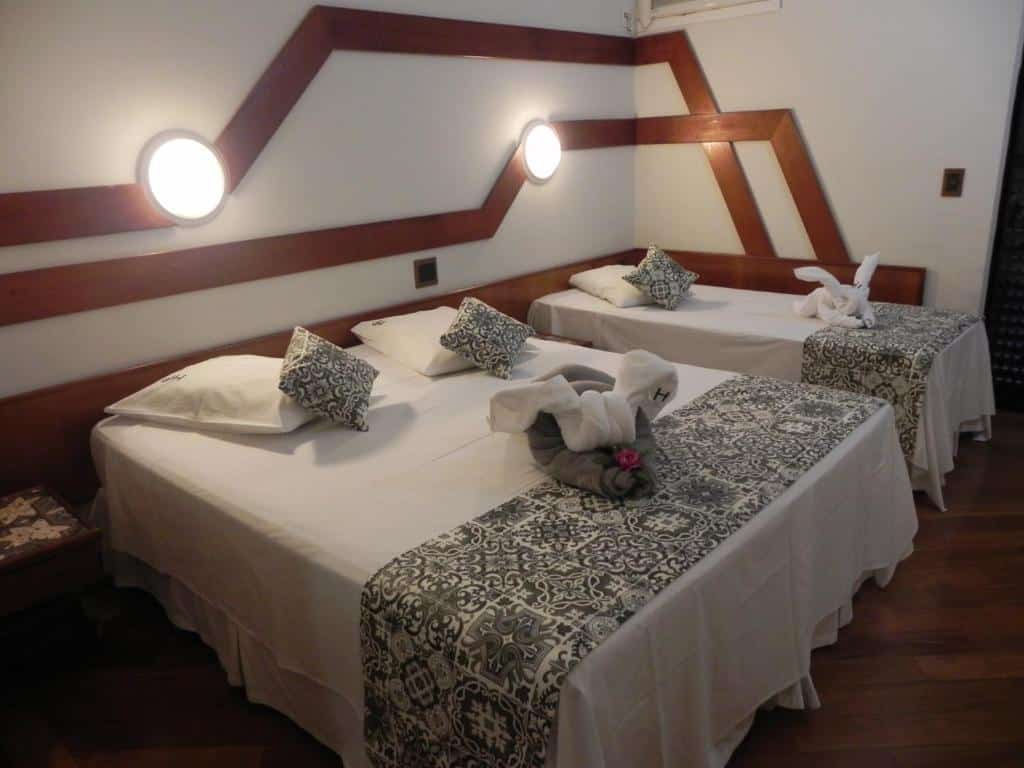Quarto do Serra Negra Paladium Hotel com uma cama de casal e uma de solteiro, há toalhas, almofadas e travesseiro sob as camas