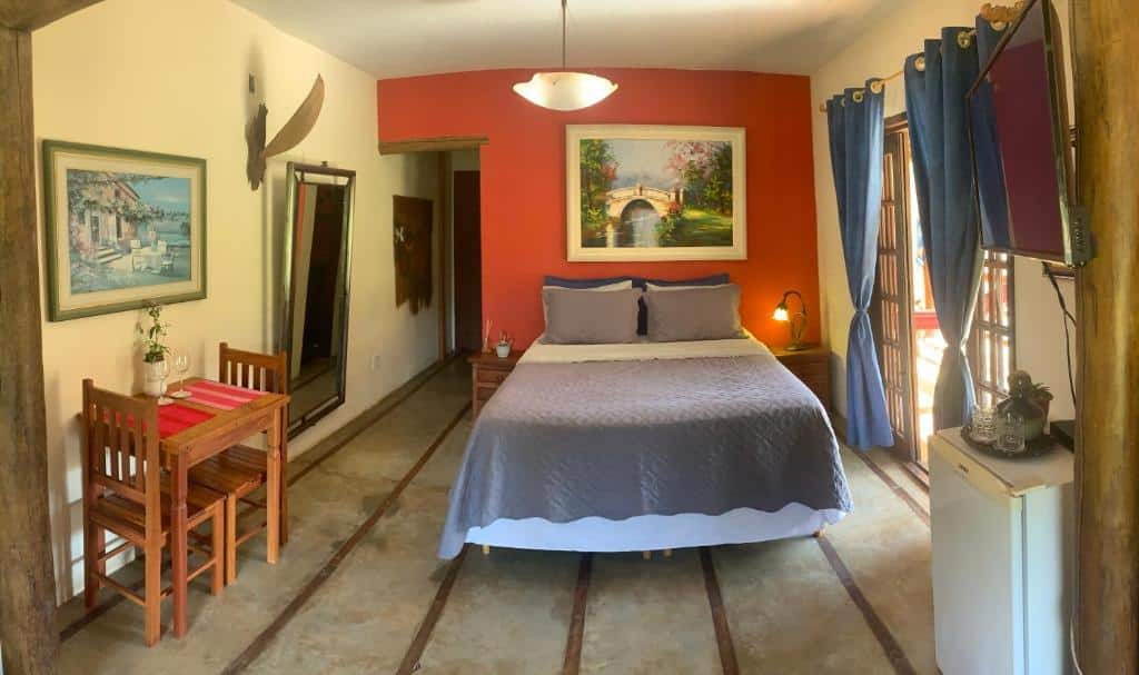 quarto amplo com cama de casal, porta grande de madeira com vista da varanda, espelho e parede avermelhada na Recanto Roça Grande