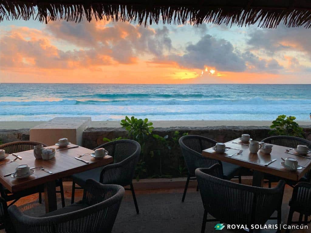 vista do sol se pondo no mar no refeitório do Royal Solaris Cancun mostrando as ondas se quebrando bem em frente as mesas e cadeiras do restaurante