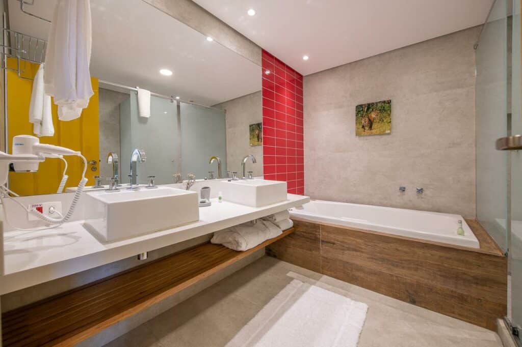 Banheiro amplo do Sandi Hotel com uma banheira, duas pias e uma prateleira com toalhas e roupões, para representar hotéis em Paraty