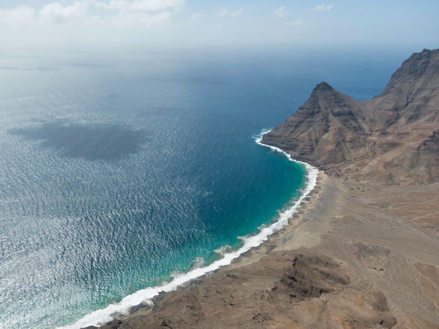 Visão aérea de mar turquesa e uma praia ao lado direito. - Foto: Secret Travel Guide via Unsplash