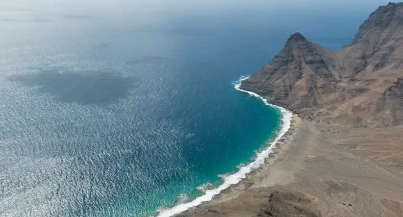 Visão aérea de mar turquesa e uma praia ao lado direito. - Foto: Secret Travel Guide via Unsplash