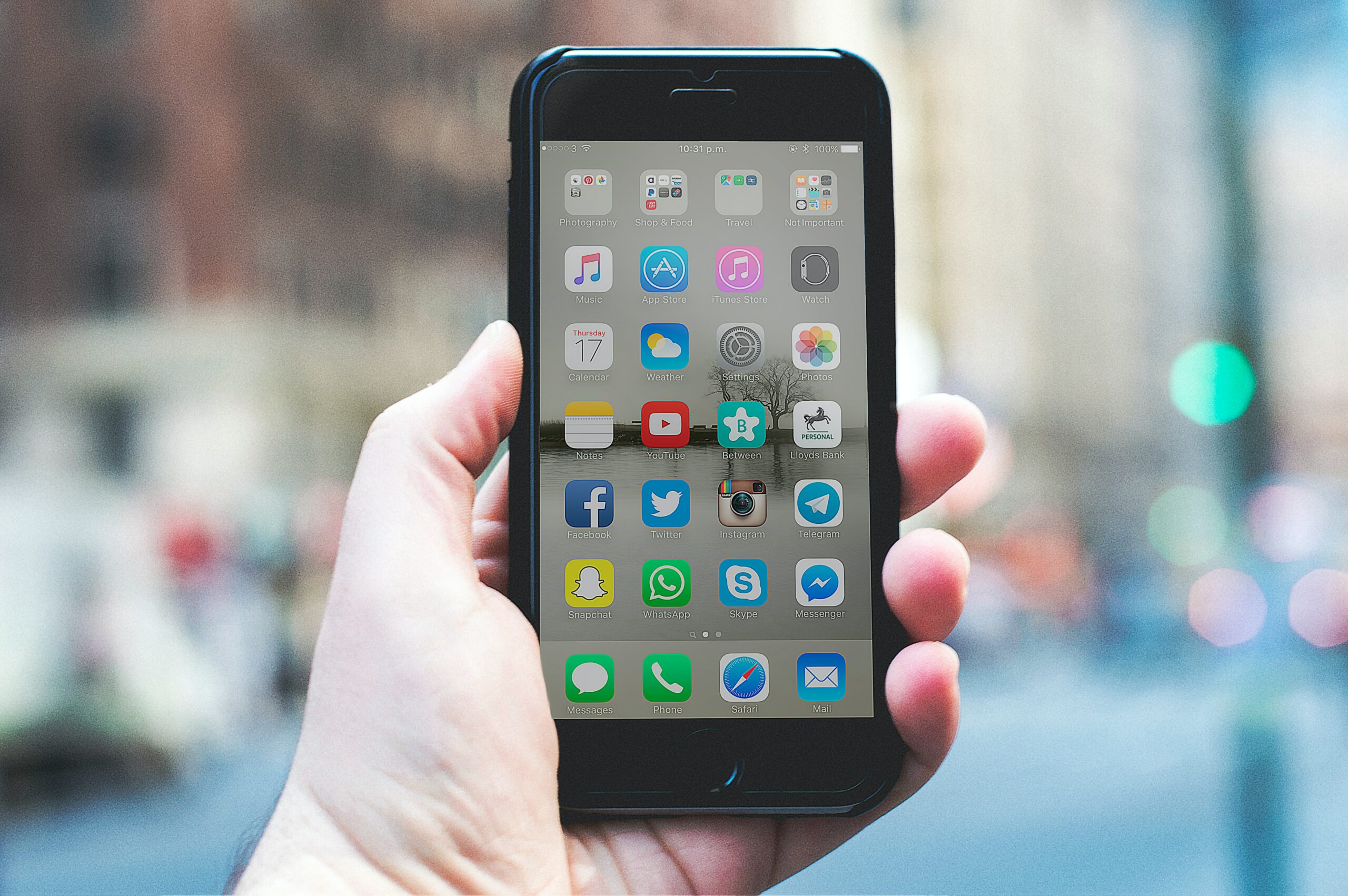 mão branca segundo um iphone preto com e tela desbloqueada e mostrando vários ícones de aplicativos.