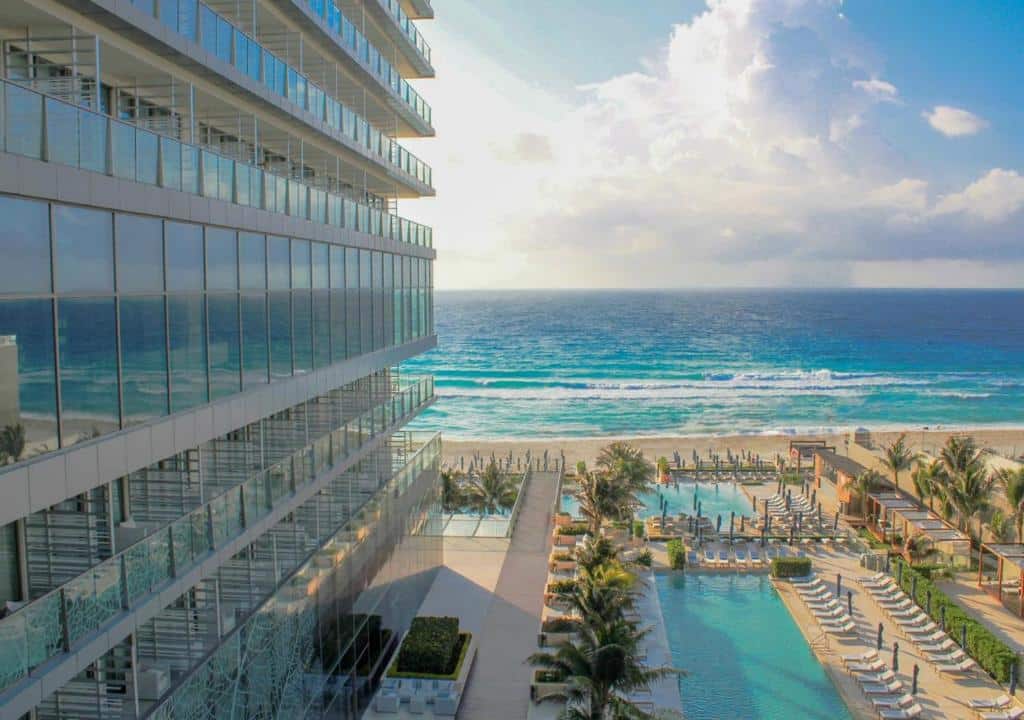 vista do mar pela janela do Secrets The Vine Cancun, mostrando a lateral do hotel, a piscina e a praia
