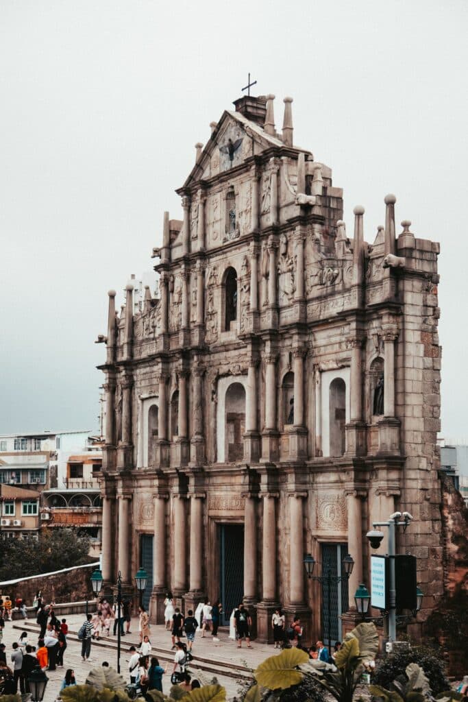 Fachada marrom de uma igreja com pessoas na frente. São as Ruínas de São Paulo para ilustrar o post seguro viagem Macau.  - Foto: Simon Zhu via Unsplash
