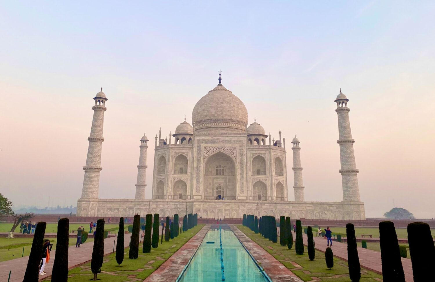 O Taj Mahal é um prédio branco de concreto. Em frente a ele há sua imagem espelhada em água. - Foto: Mike Swigunski via Unsplash