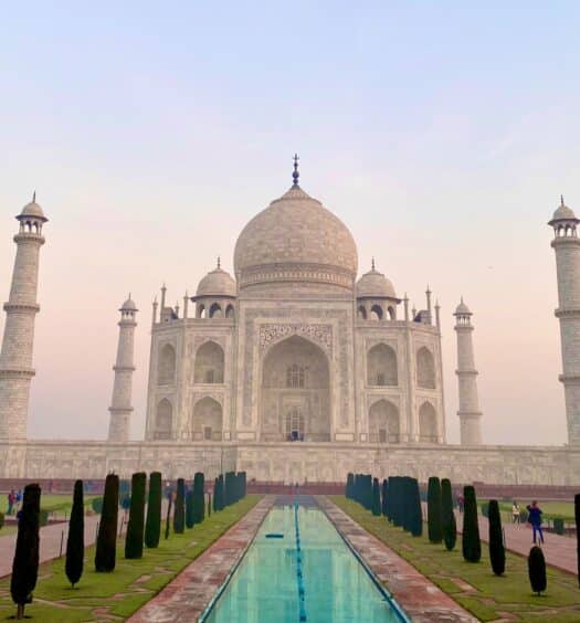 O Taj Mahal é um prédio branco de concreto. Em frente a ele há sua imagem espelhada em água. - Foto: Mike Swigunski via Unsplash