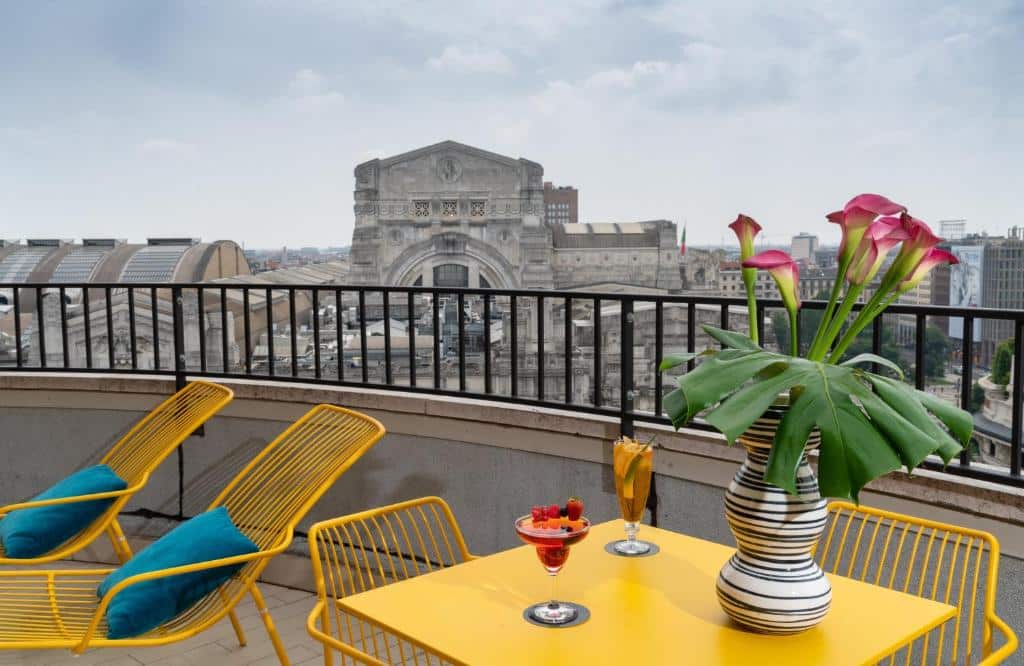 terraço com espreguiçadeiras e mesinha amarelas, uma flor, duas taças e vista para um monumento e o céu no NYX Hotel Milan by Leonardo Hotels, um dos hotéis em Milão