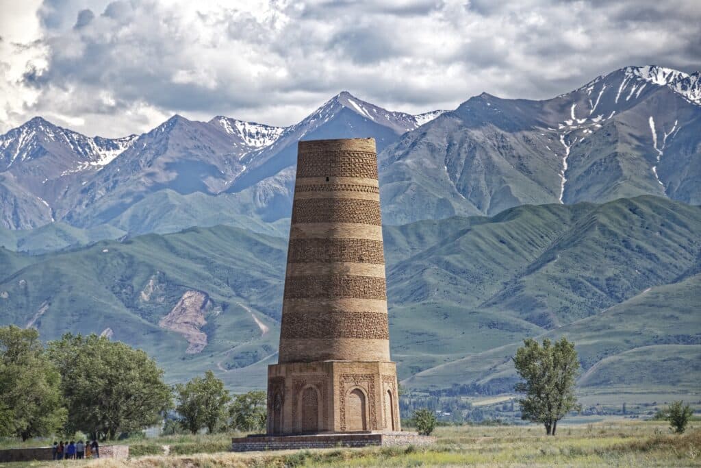 Torre marrom com árvores ao lado e montanhas ao fundo para ilustrar o post seguro viagem Quirguistão. Foto: Makalu via Pixabay