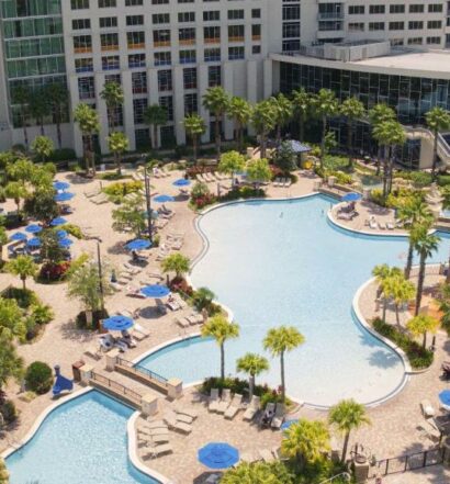 vista de cima do Hyatt Regency Orlando com uma piscina enorme, ponte ligando os dois lados, com árvores e o prédio do hotel mais ao fundo, para ilustrar o post sobre hotéis em Orlando