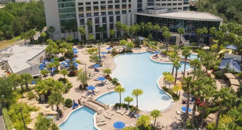 vista de cima do Hyatt Regency Orlando com uma piscina enorme, ponte ligando os dois lados, com árvores e o prédio do hotel mais ao fundo, para ilustrar o post sobre hotéis em Orlando